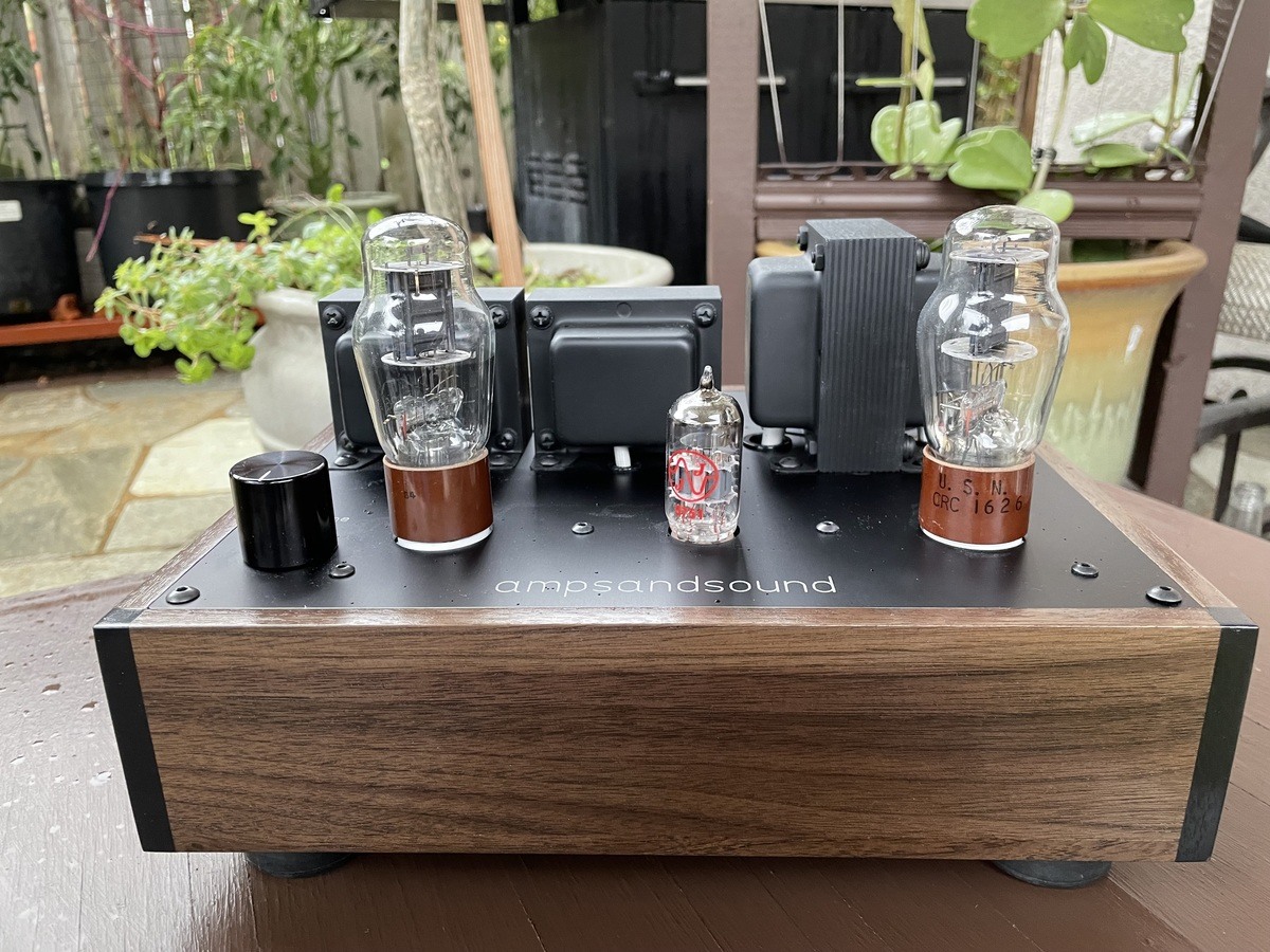 A photo of the ampsandsound Kenzie OG Rev 2 on a wooden table in yard with plants in the background